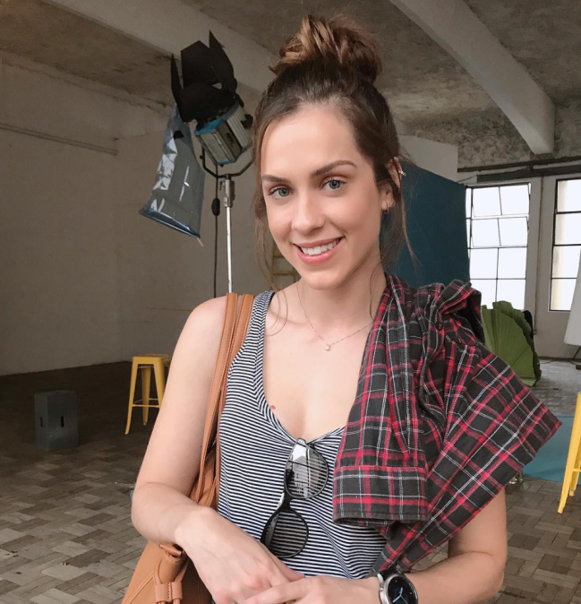 Sophia Abrahão com coque bagunçadinho, sorridente, usando regata cinza e óculos pendurado na blusa.