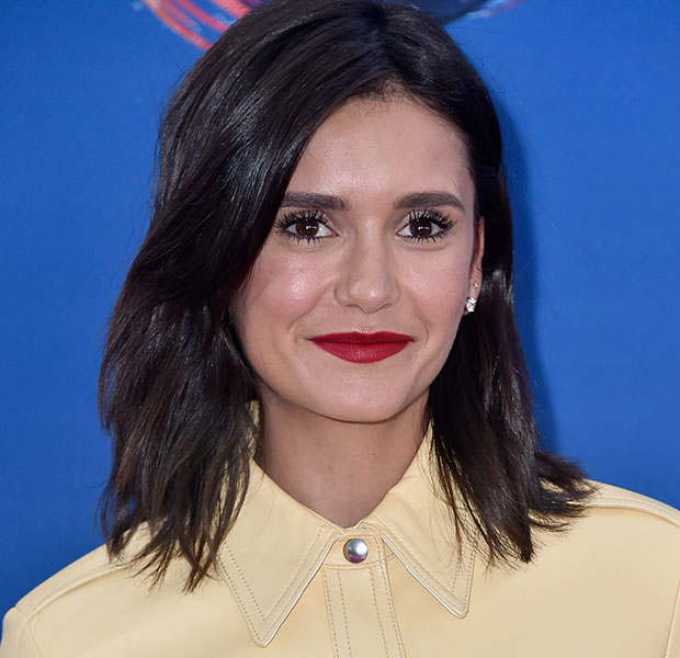 Nina Dobrev sorridente posando para foto e usando camisa amarela.