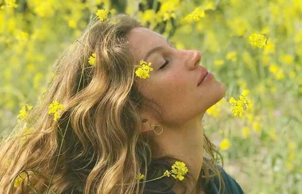 Foto de Gisele rodeada por flores amarelas; ela está de olhos fechados inclinando a cabeça e algumas flores estão em seu rosto