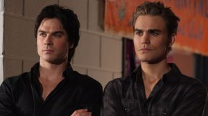 Ian Somerhalder e Paul Wesley em cena de The Vampire Diaries; os dois usam roupas pretas e estão encarando alguém com expressão séria e os braços cruzados na frente do peito