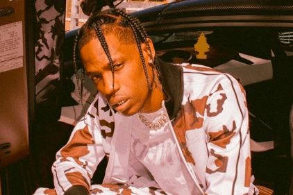 Travis Scott posando para foto com corpo curvado e roupa branca com detalhes em marrom