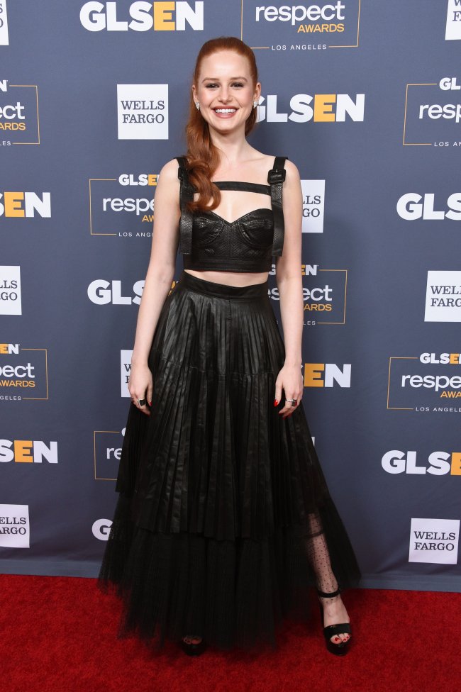 Madelaine Petsch usando conjuntinho preto em carpet; ela está com o cabelo semipreso, sorrindo, com os braços estendidos ao lado do corpo