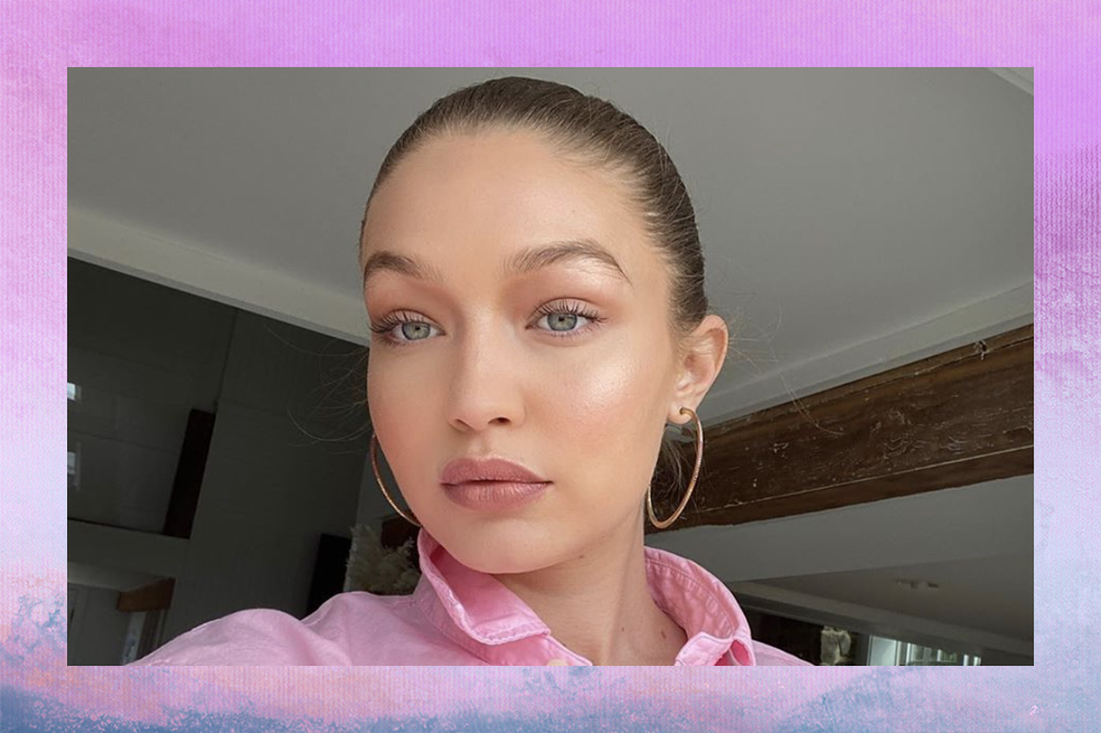 Gigi Hadid em selfie com cabelo preso, brincos de argola e blusa rosa