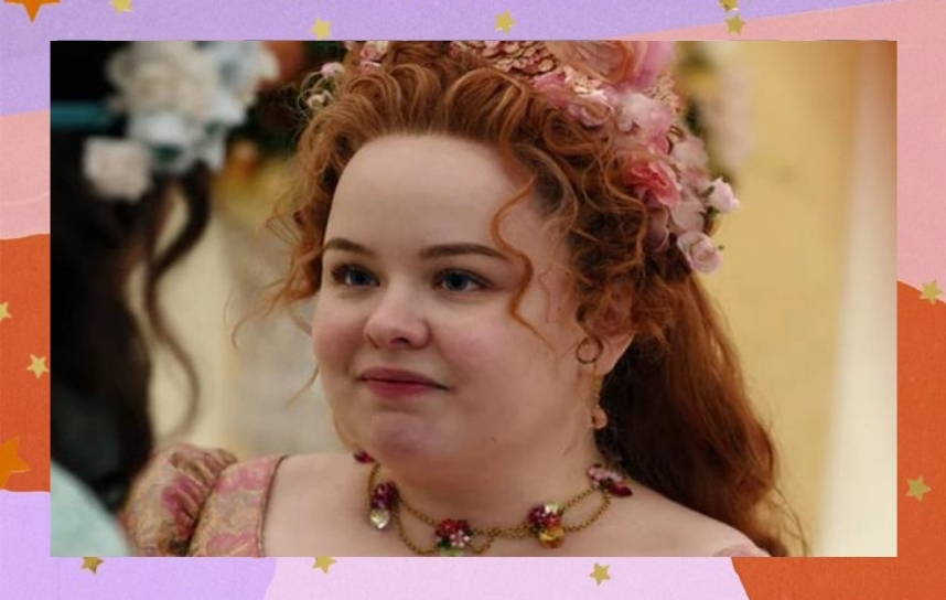 personagem Penelope, de Bridgerton. Ela usa um colar, flores no cabelo e está dando um sorriso um pouco forçado