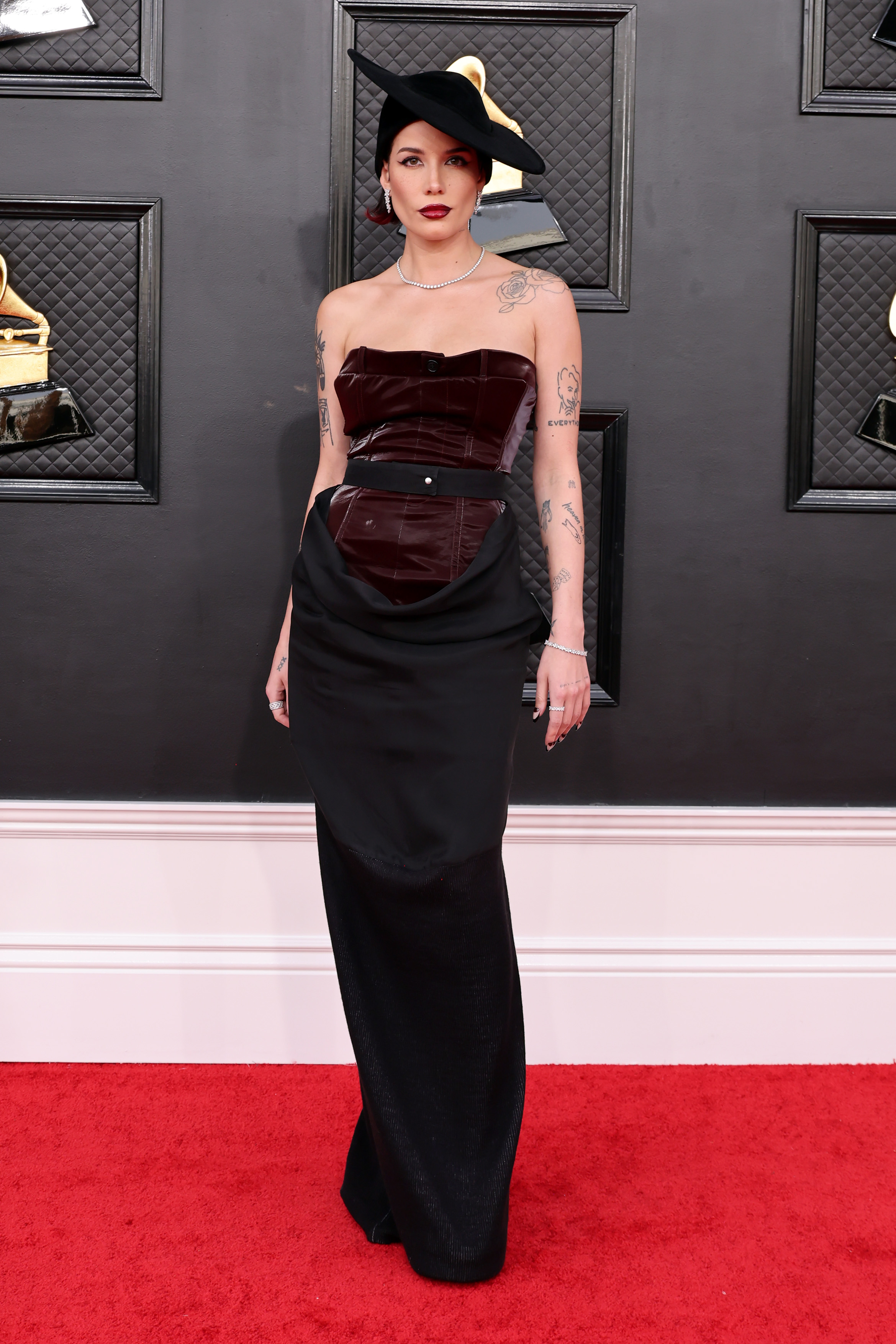 Imagem mostra Halsey no tapete vermelho da 64ª edição do Grammy Awards usando um vestido tomara que caia marrom e preto Pressiat, acompanhado de chapéu Pierra Cardin dramático, inclinado e de aba larga.