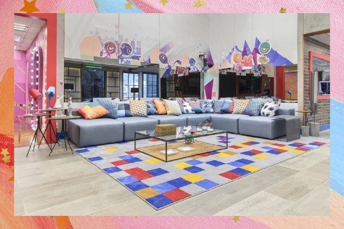 Sala do Big Brother Brasil. com um grande sofá cinza, um tapete e uma mesa de centro