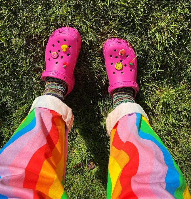 Foto mostrando somente parte da calça colorida com crocs rosa com pingente colorido de smile e frutas