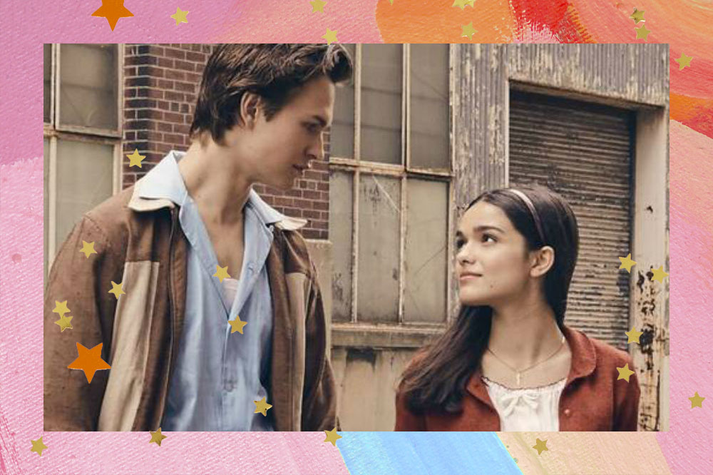 Ansel Elgort e Rachel Zegler em cena do filme Amor, Sublime Amor; os atores estão olhando um para o outro, ele usa uma camisa azul clara com casaco marrom e ela uma blusa branca com casaco vermelho