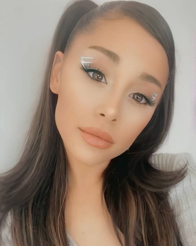 Ariana Grande a cabeça levemente inclinada com com uma expressão levemente séria, na imagem só conseguimos ver seu rosto e um pouco do seu cabelo sem detalhes da sua roupa