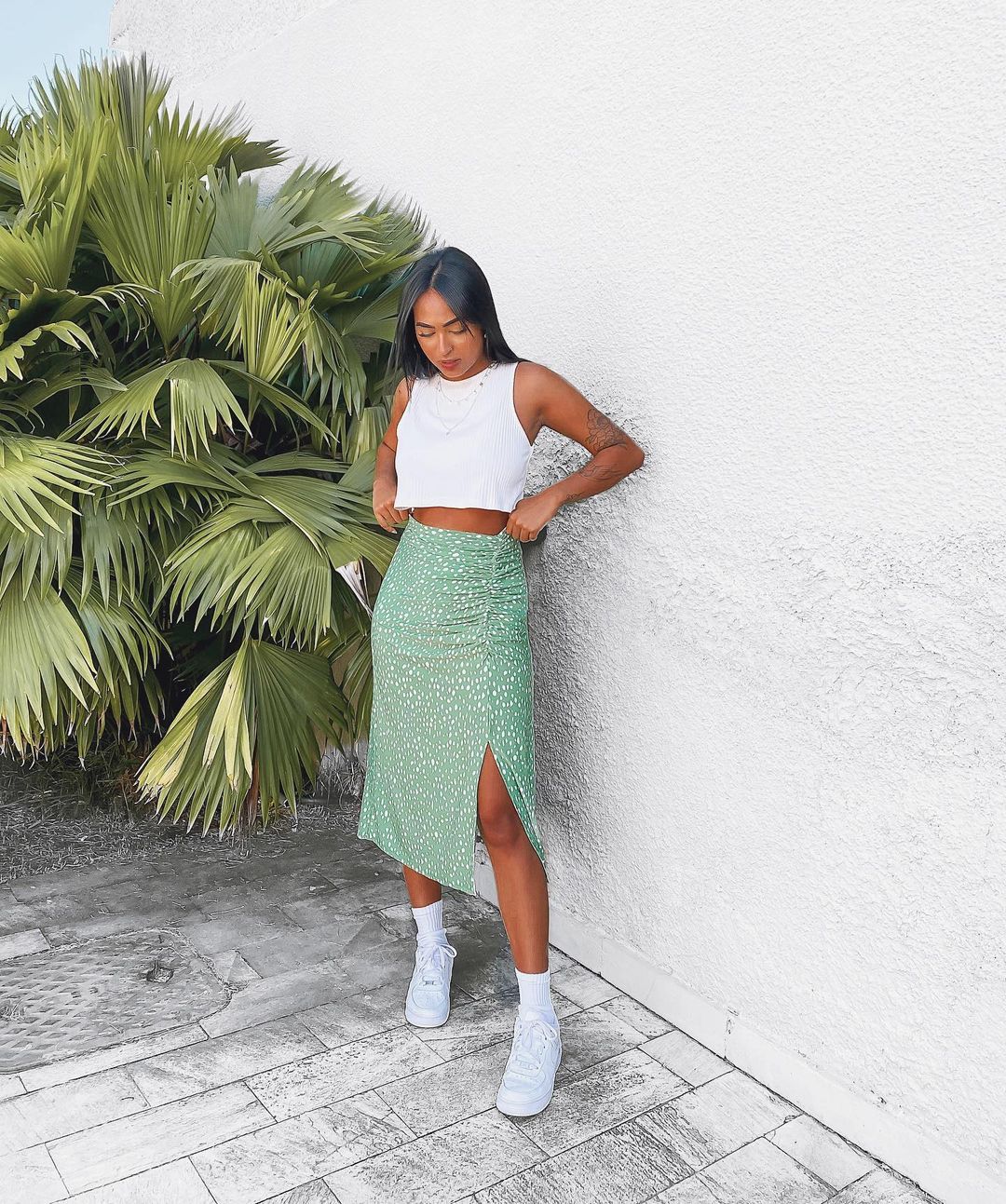 look-top-cropped-branco-brendapabreu- Garota usando top cropped branco com saia midi verde com bolinhas brancas e tênis e meia brancos. Ela está olhando para baixo com as duas mãos arrumando a blusa.
