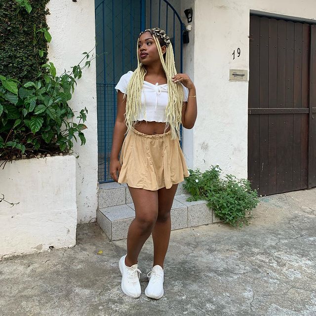 look-top-cropped-branco-juhmarquesf Garota usando top cropped branco com saia bege e tênis branco. Ela está olhando para os lados com uma das mãos no cabelo comprido.