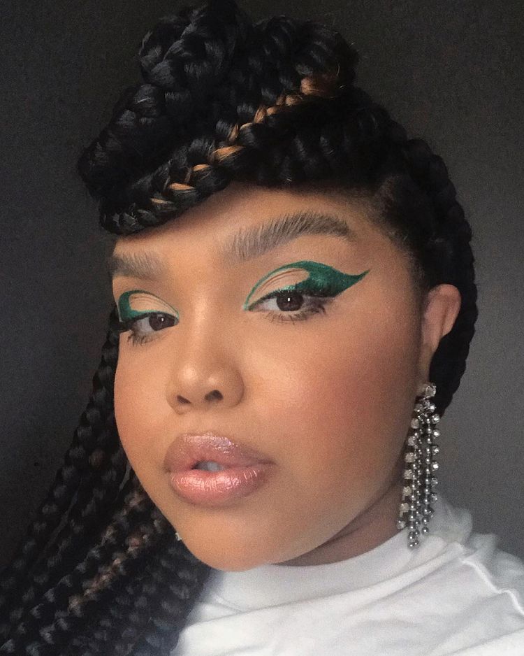 maquiagem-olho-verde-angelic4silva Garota usando maquiagem com delineado gráfico verde escuro. Na foto, só dá para ver o rosto com blush marcado, batom cor de boca e brinco de strass. Sua expressão facial é séria, com a boca levemente aberta.