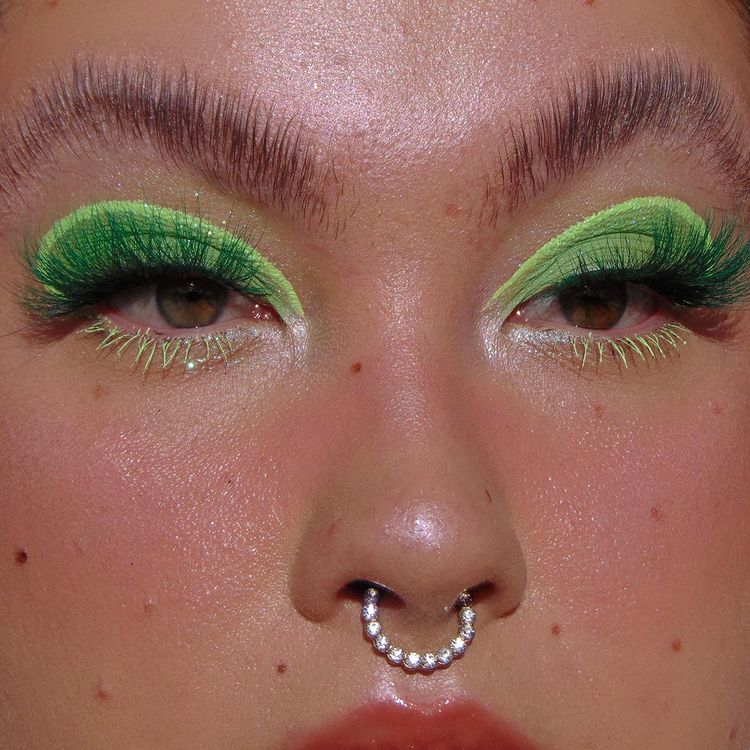 maquiagem-olho-verde-makeupbylourose Garota usando maquiagem com dois tons de sombra verde: um mais escuro e outro mais claro. Na foto, dá apenas para ver o seu rosto. Suas sobrancelhas estão penteadas para cima, sua pele tem sardas, ela usa um piercing no septo e olha para a lateral.