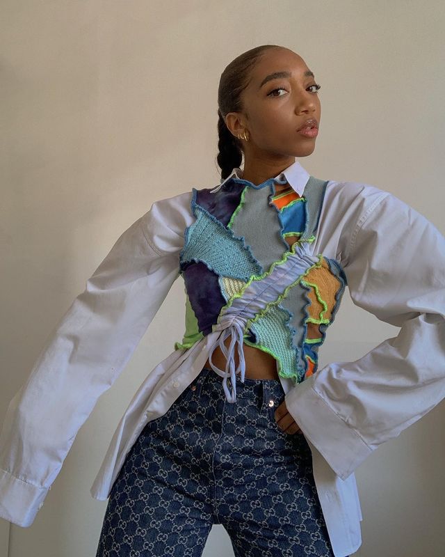 tendencia-patchwork-soleneoj Garota usando blusa cropped de patchwork sem mangas e nas cores azul, roxo, amarelo, verde neon e laranja, por cima de uma camisa branca oversized. Ela ainda está com uma calça jeans com estampa do logo da Gucci. Uma das mãos está no bolso e sua expressão facial é séria, com a cabeça levemente inclinada para o lado.