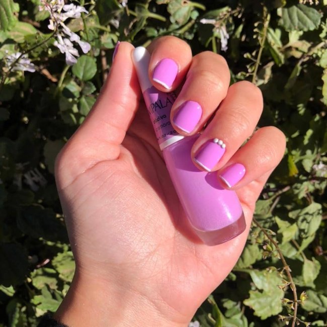 Foto mostrando uma mão com os dedos dobrados para evidenciar as unhas pintadas em francesinha colorida nas cores rosa e branco.