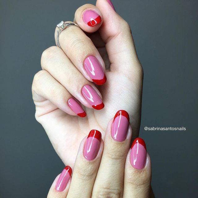 Foto mostrando uma mão com os dedos dobrados para evidenciar as unhas pintadas em francesinha colorida nas cores rosa e vermelho.
