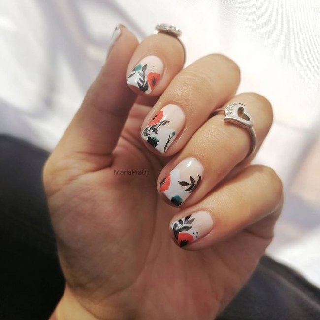 Nail art com flores e folhagem Dedos dobrados com anel exibindo nail art com base clara e detalhes laranja e preto.