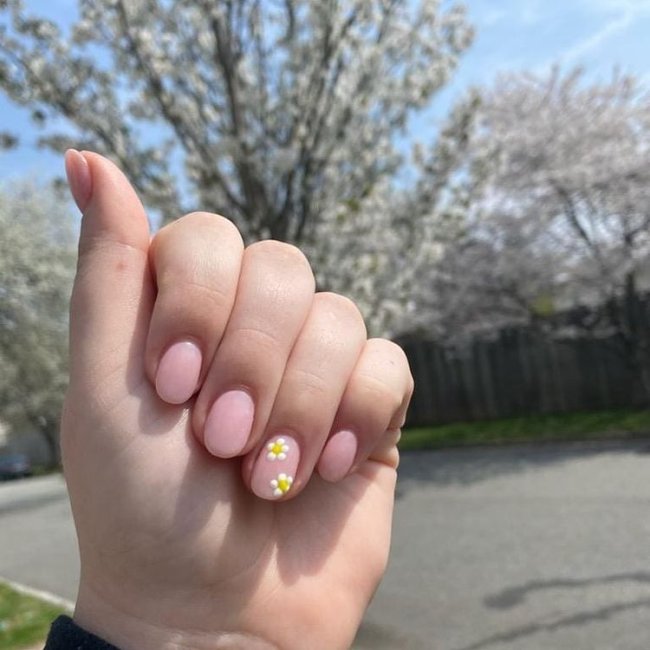 Mão com os dedos dobrados exibindo as unhas com florzinha branca.