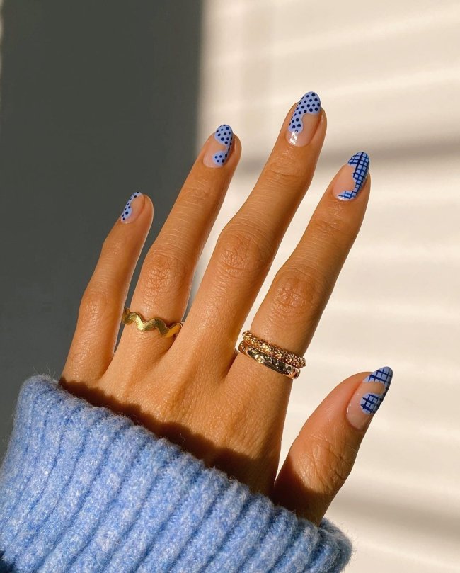 nail art azul Foto de uma mão com anéis no dedo anelar e indicador. As unhas estão pintadas com uma nail art ondulada, estampa xadrez e bolinhas.