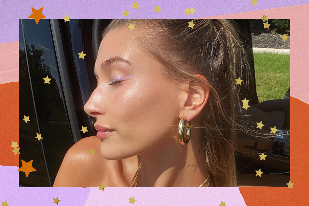 Montagem com foto da Hailey Bieber usando brinco de argola. Ela está de olhos fechados, com a cabeça virada para o lado e dá para ver um brinco dourado de argola em sua orelha. O fundo da montagem é lilás, rosa e laranja e há estrelinhas laranjas e amarelas.