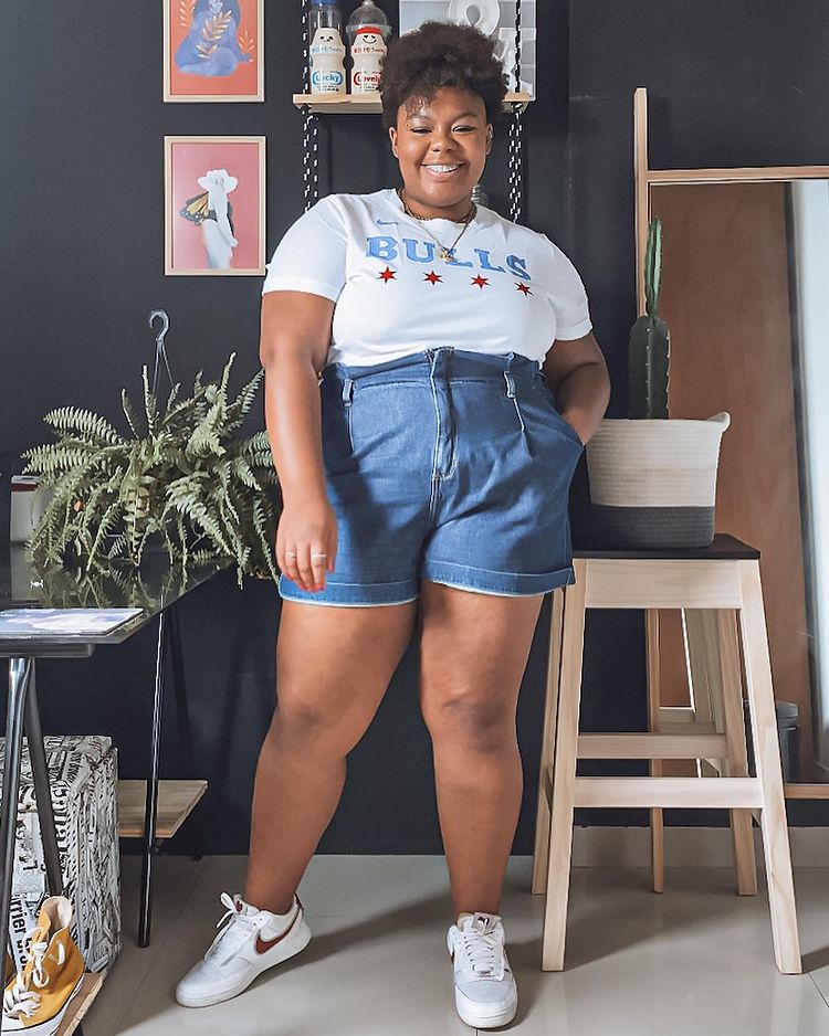 camiseta-branca-short-jeans-marinhoje Garota usando camiseta branca, short jeans de cintura alta e tênis branco com detalhe em vermelho. Ela está sorrindo e com uma das mãos no bolso.