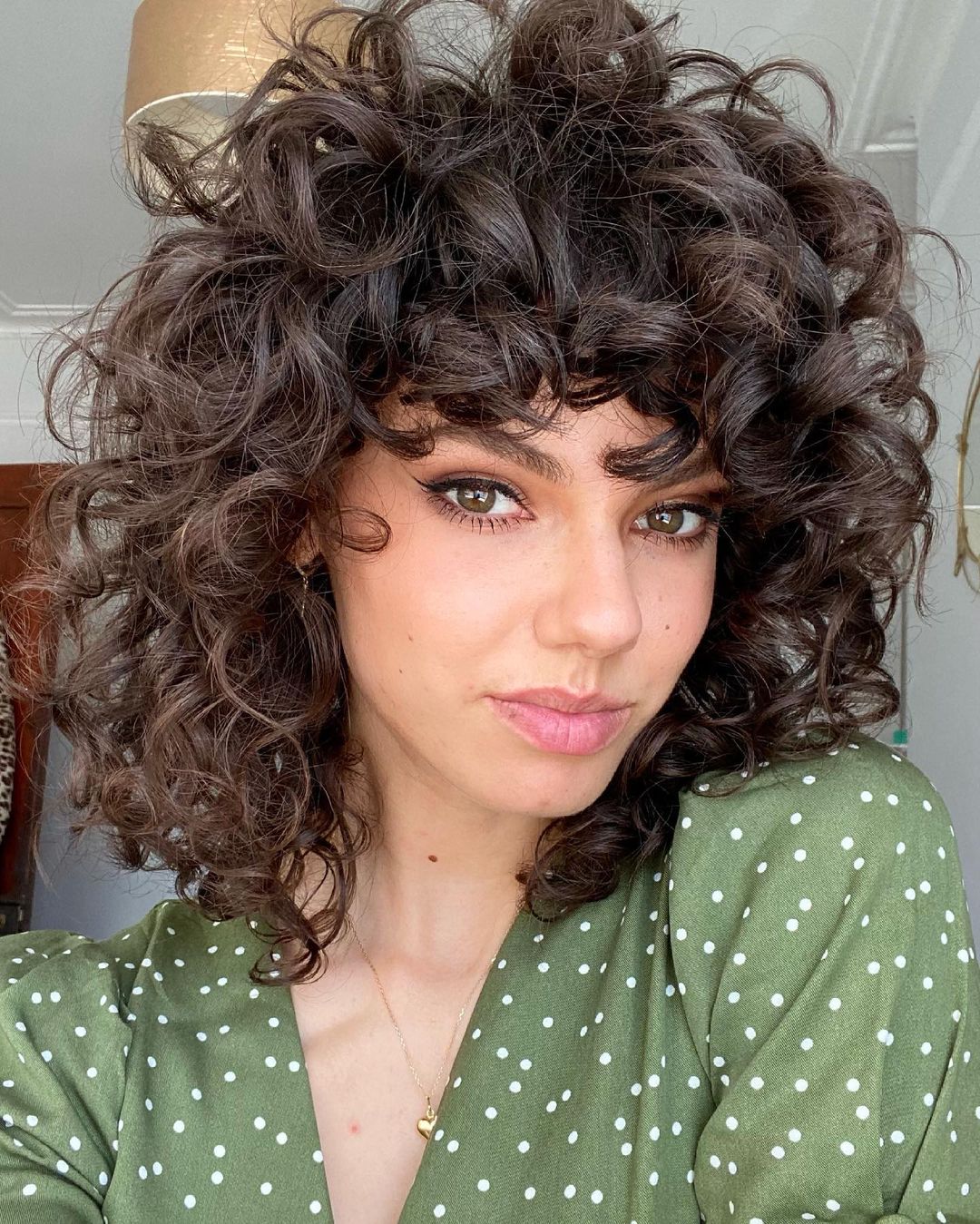 long bob com franja Jovem com expressão levemente sorridente, exibindo seu corte bob, usando blusa verde com bolinhas.