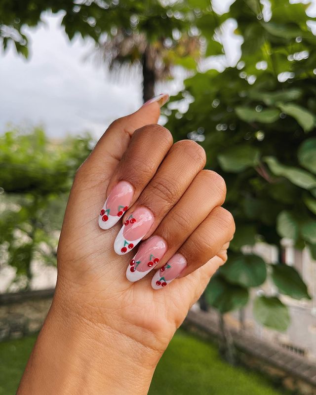 Foto com destaque nas unhas com nail art de bolinha, dessa vez formando uma cereja vermelha na ponta da unha.