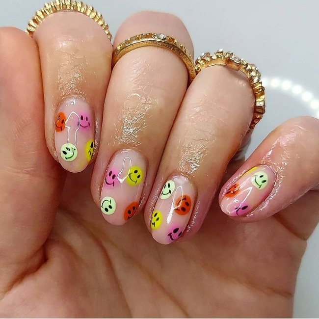 Foto com destaque nas unhas com nail art de bolinha, dessa vez formando smiles coloridos, nas cores laranja, roxo e verde.