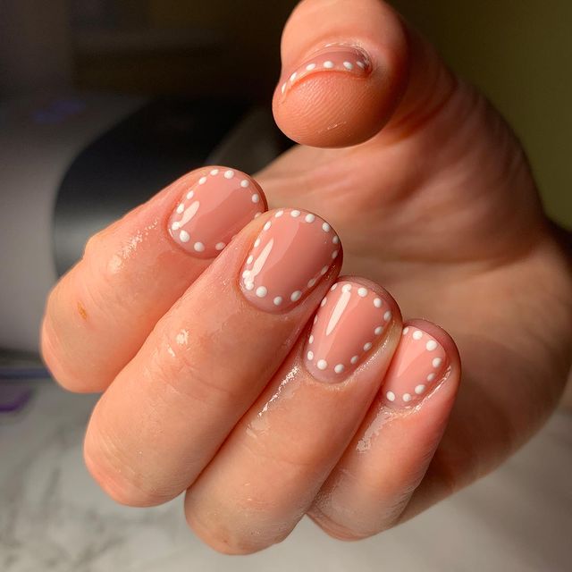 Foto com destaque nas unhas com nail art de bolinha, dessa vez com bolinhas brancas ao redor da unha.