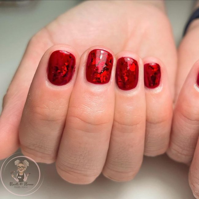 Unha vermelha com glitter Foto com close em uma mão fechada mostrando os dedos, nas unhas esmalte vermelho com glitter.