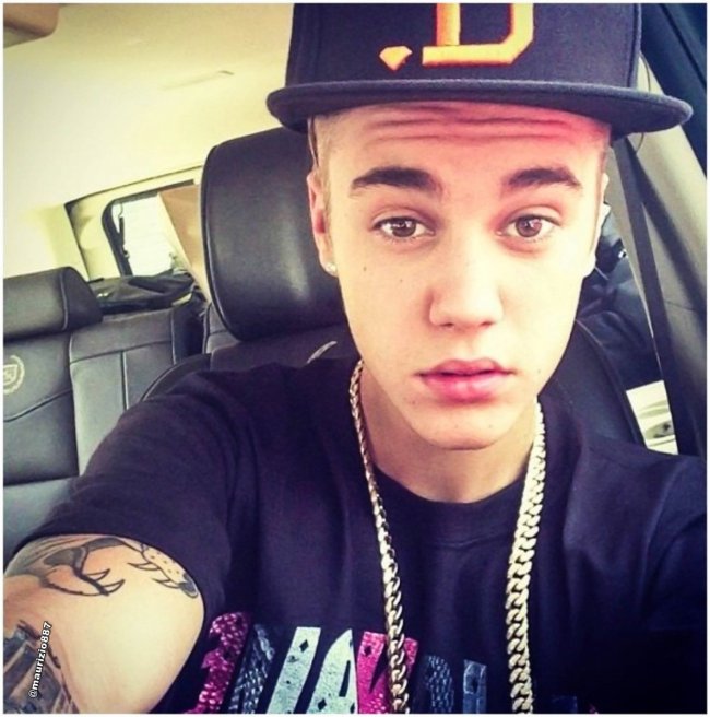 bone-de-aba-reta-jb Selfie do cantor Justin Bieber. Ele usa uma camiseta preta, corrente dourada e boné de aba reta. Olha para a câmera mas não sorri.