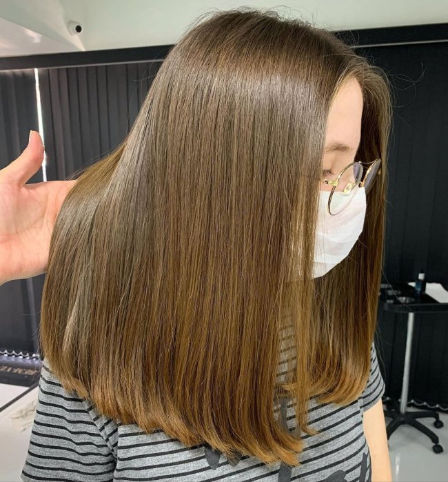cabelo com corte reto Jovem com a cabeça abaixada, usando blusa listrada, alguém está levantando uma parte de seu cabelo.