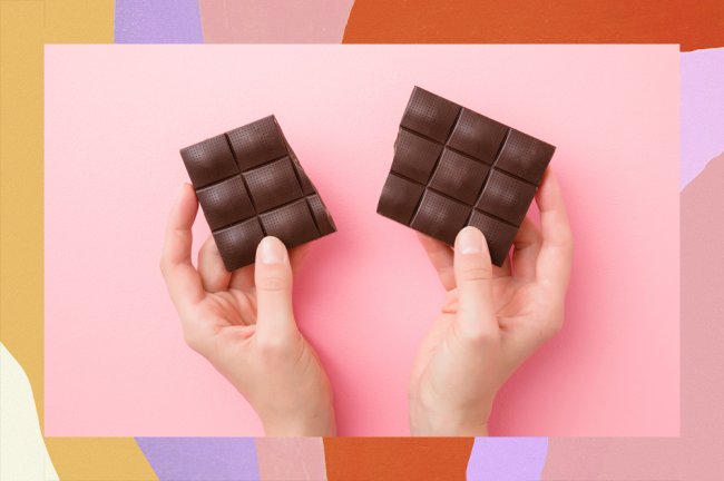 Uma mão segurando um tablete de chocolate amargo sobre um fundo rosa