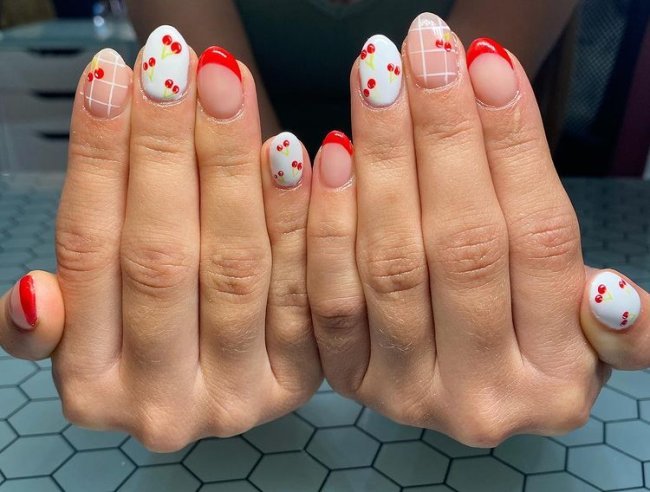 unhas decoradas com esmalte vermelho Foto com foco nas mãos exibindo a nail art das unhas. No caso, unhas brancas com detalhes em vermelho e cerejas.
