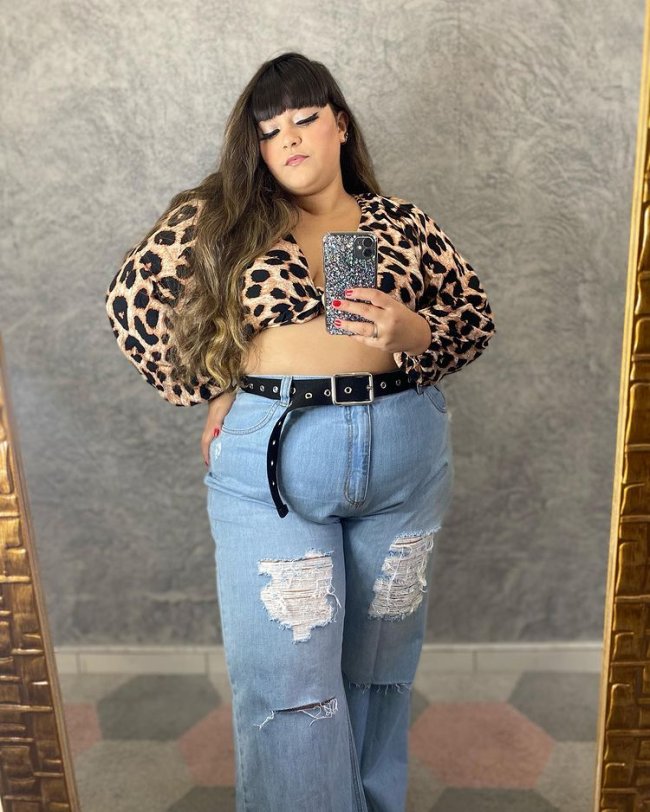 Jovem tirando selfie em frente a espelho usando top com animal print e calça wide leg.