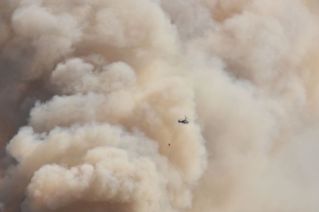 Foto de uma imensa nuvem marrom e de um helicóptero pequenininho sobrevoando na frente dela