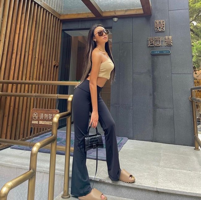 chinelo nuvem Jovem posando em escada com cropped bege e calça preta. Sua expressão é séria.