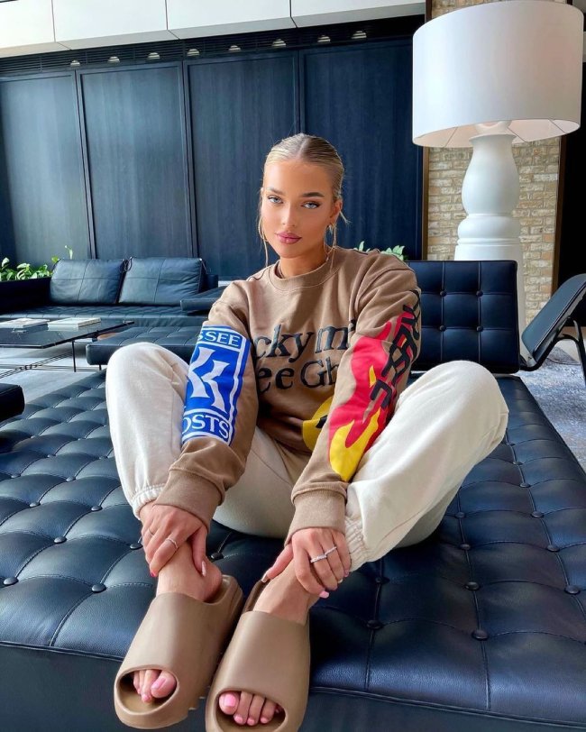 look com chinelo nuvem marrom Jovem sentada posando com as mãos nos calcanhares usando blusa de moletom e calça bege.