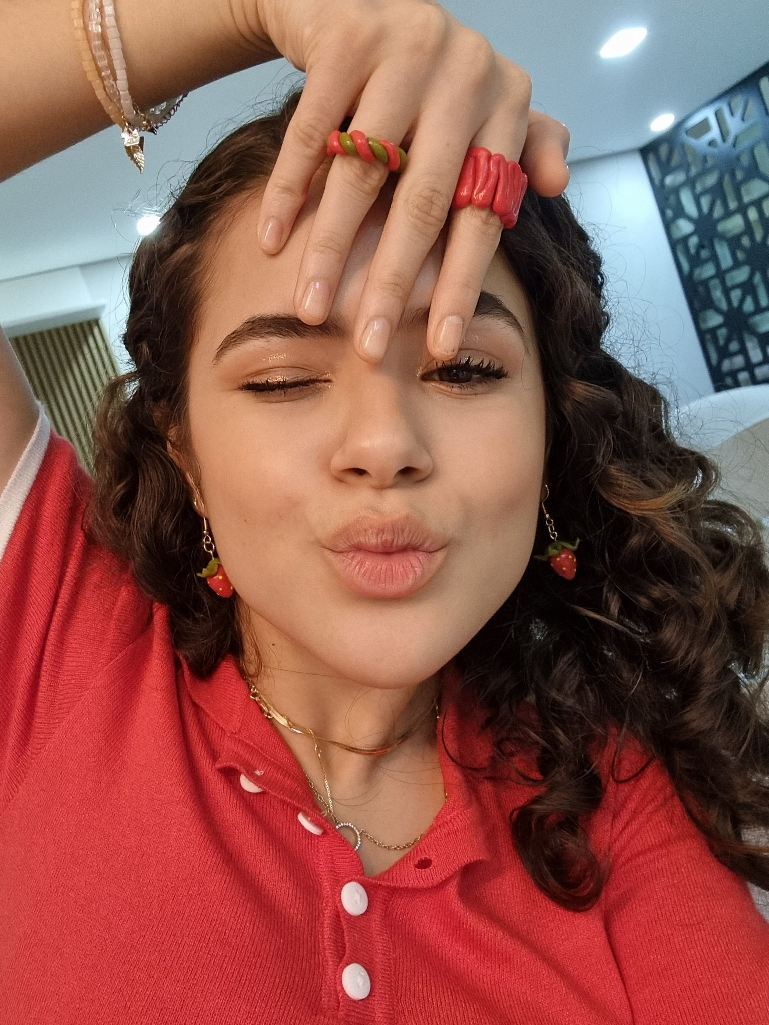 maisa-silva-acessorios-aneis Maisa Silva com um dos olhos fechados, fazendo biquinho, usando blusa vermelha e uma das mãos na testa com anéis vermelhos nos dedos
