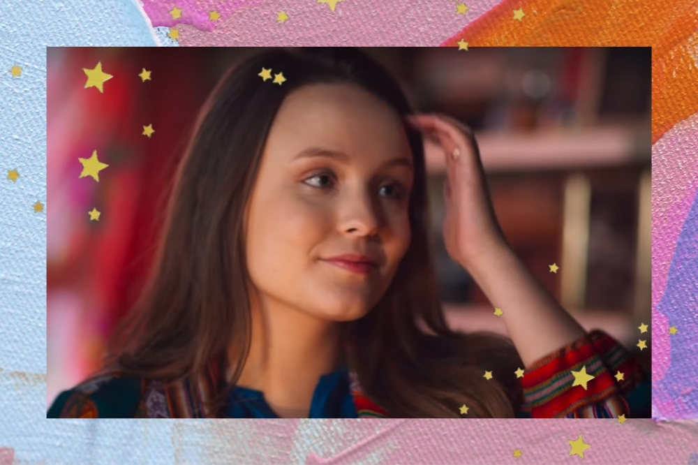 Montagem com o fundo azul, roxo e laranja com detalhes de estrelinhas douradas com a imagem da Larissa Manoela no trailer de Modo Avião