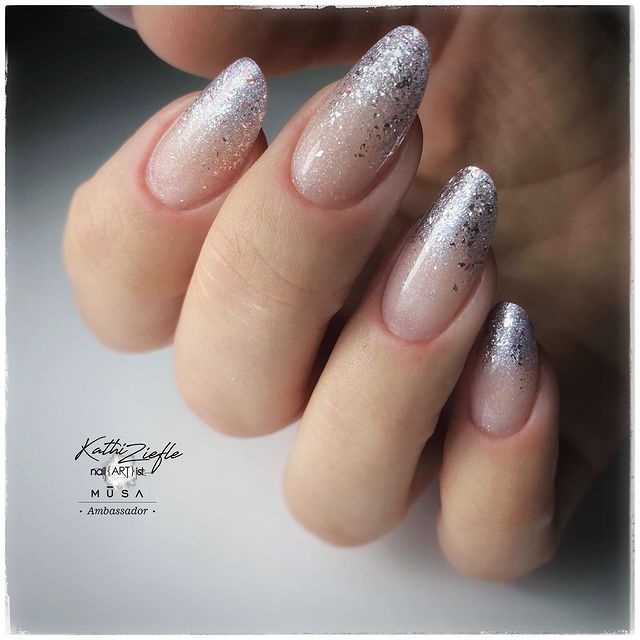 Foto de uma mão com foco nas unhas decoradas no estilo baby boomer com um glitter prata.