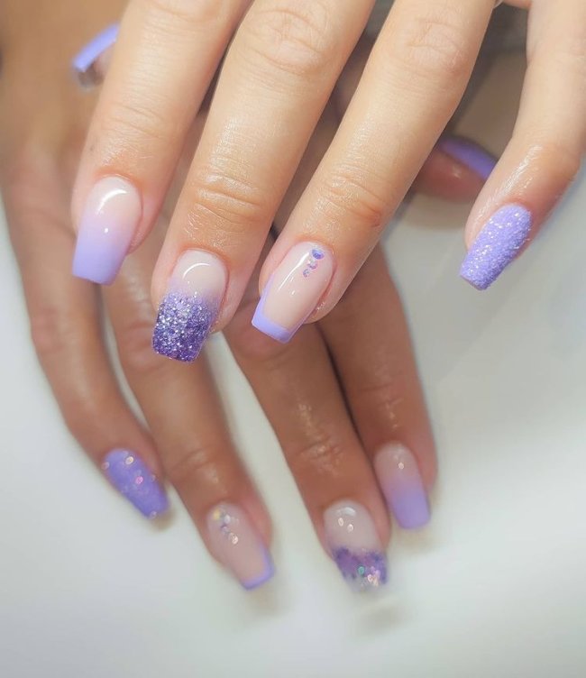 unha-baby-boomer-lilas Foto de uma mão com close nas unhas decoradas no estilo baby boomer na cor lilás com detalhes de pedrinhas na unha do dedo anelar.