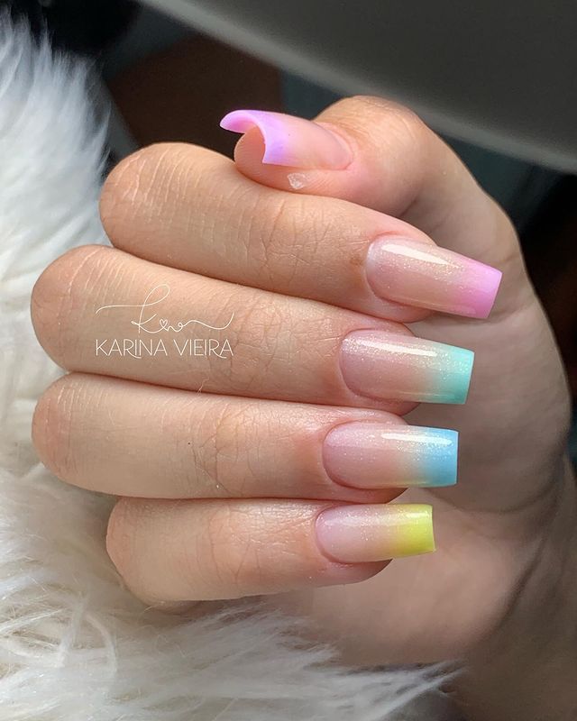 unhas-baby-boomer-cores Foto de uma mão com foco nas unhas decoradas no estilo baby boomer nos tons de liás, rosa, azul claro, azul escuro e amarelo.