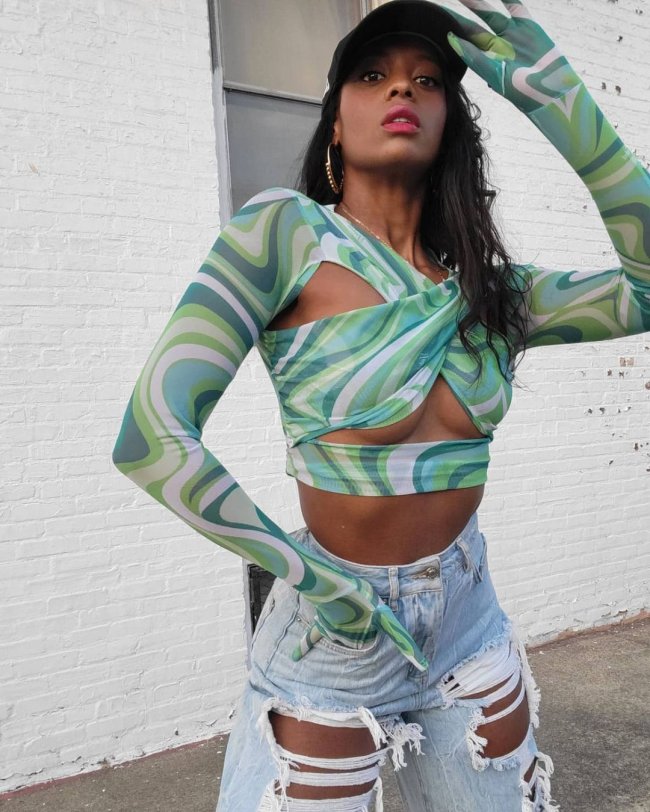 blusa verde com recortes Jovem posando com uma mão no short e a outra na cabeça. Ela usa blusa verde com recorte.