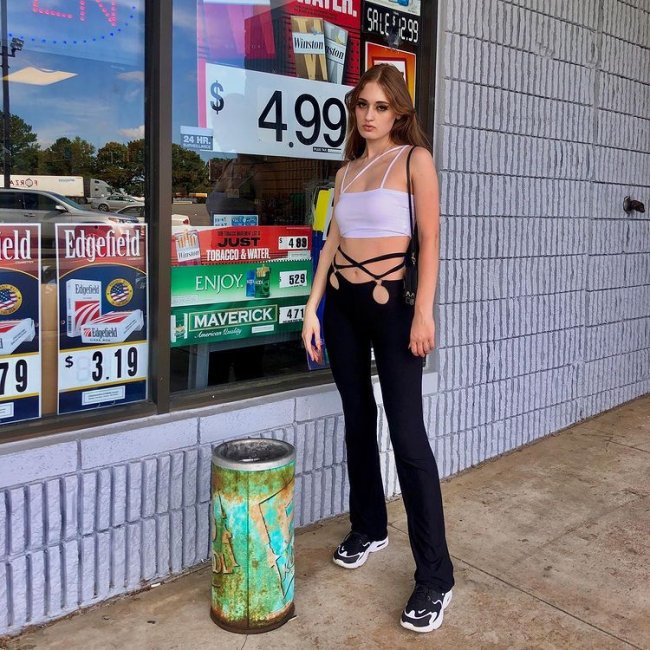 Jovem posando em frente a loja com expressão séria e usando calça com recorte.