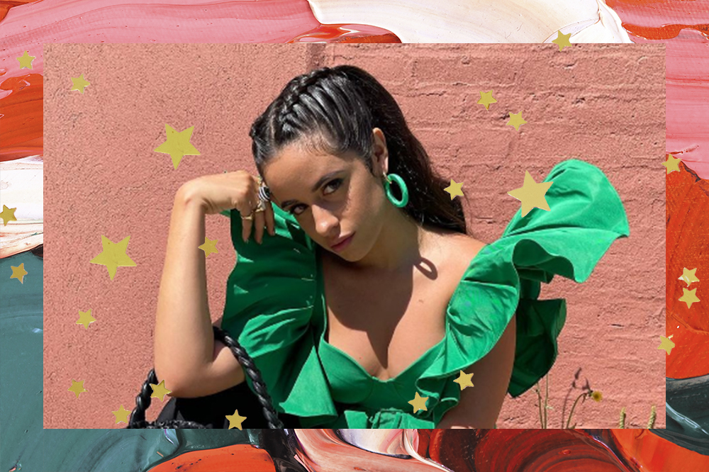 Camila Cabello usando top cropped verde, brinco de argola verde, com expressão facial séria e um dos braços dobrados com a mão próxima ao rosto