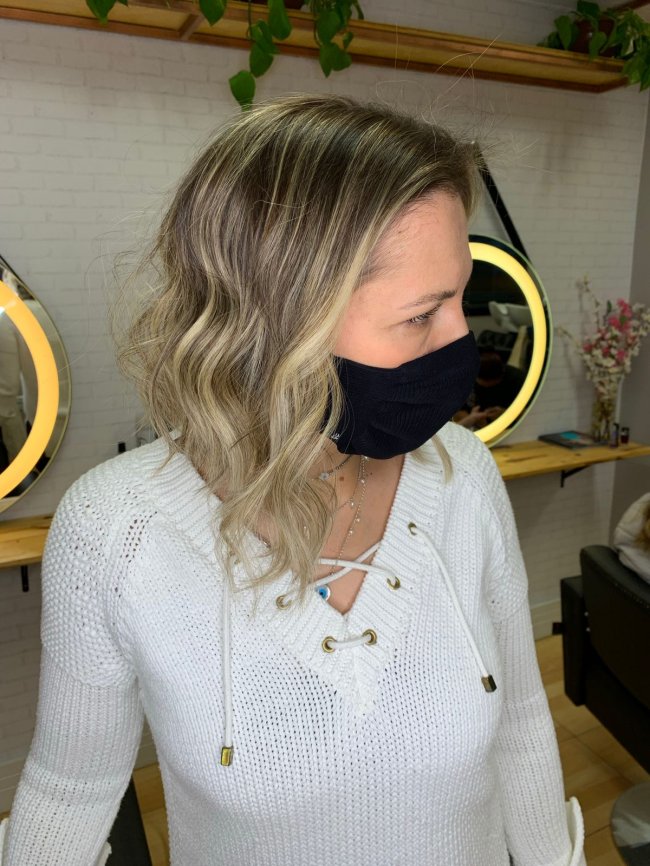 Corte cabelo repicado Mulher com o rosto virado para o lado direito e usando blusa branca. Atrás dela, podemos ver espelhos pendurados na parede.