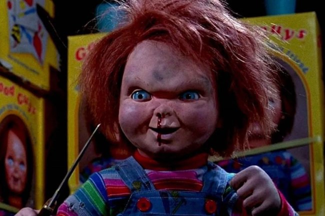 Foto do Chucky, o brinquedo assassino. Ele é ruivo, usa um macacão jeans, segura uma adaga e tem sangue escorrendo do nariz