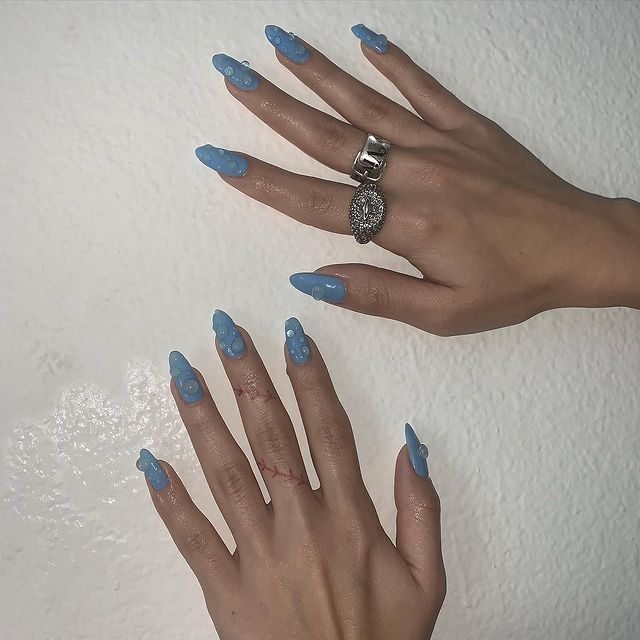 Foto de duas mãos com as unhas longas pintadas de azul e detalhe 3D imitando gotas de água.