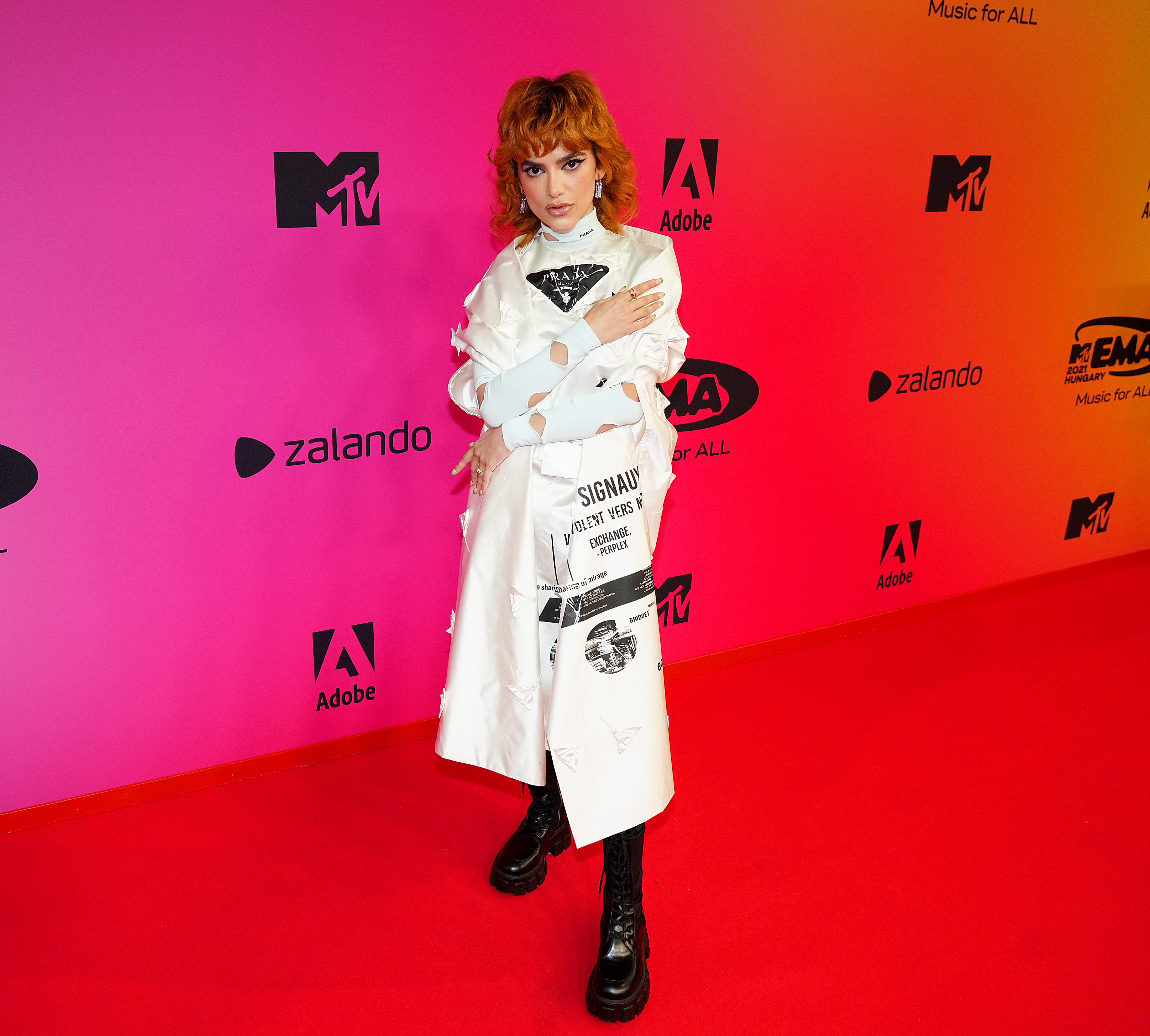 Manu Gavassi posando com look branco e bota preta em frente a parede do red carpet durante o MTV EMA na Hungria.